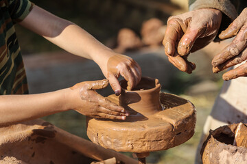 Hands of a boy and a man sculpt clay dishes.