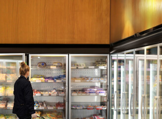 Woman choosing frozen food from a supermarket freezer. purchasing a packet of meat at the supermarket