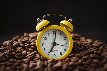 Yellow vintage alarm clock on the black background in the middle of coffee beans pile. shallow...