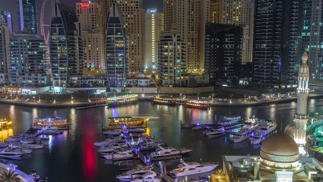 Yachts in Dubai Marina flanked by the Al Rahim Mosque and residential towers and skyscrapers aerial day to night transition timelapse. Modern high rise skyline with boats and wooden dhows