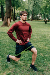 Handsome sportsman doing lunges while training with resistance band in park