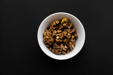 Walnut in a small plate on a black table. Walnuts is a healthy vegetarian protein nutritious food. Natural nuts snacks.