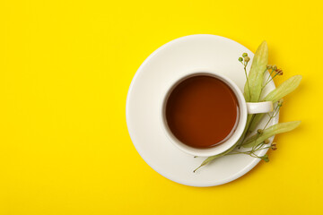 Cup of linden tea on yellow background, top view