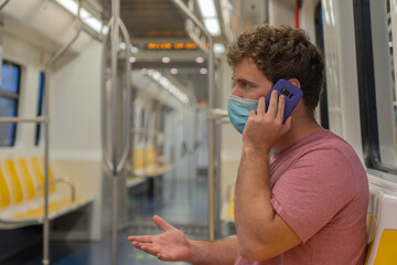 Public transport, young man traveling inside the train sitting keeping safety distance and mask, sitting using the phone