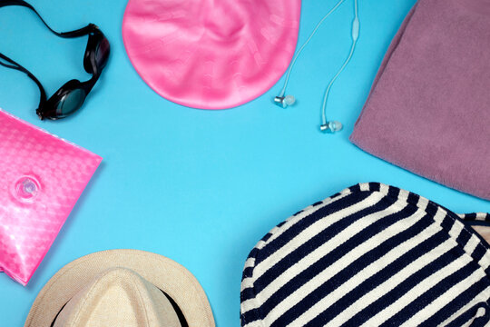 Flat lay composition with Goggles, swimming cap, backpack, Headphones, towel and Inflatable armband on blue background.