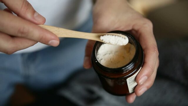 Closeup view of young woman is showing eco-friendly toothpaste in home room iroi. American female scoops organic powder for oral hygiene, holding wooden brush in her hand. Modern person demonstrates
