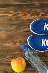 An apple, sneakers and bottle of water on wooden background with copy space for text. The concept of healthy lifestyle and fitness