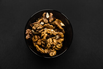 Obraz na płótnie Canvas Walnut in a small plate on a black table. Walnuts is a healthy vegetarian protein nutritious food. Natural nuts snacks.