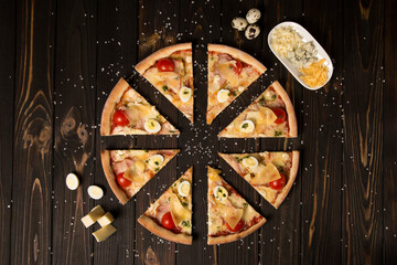 Top view of pizza with tomatoes, pesto sauce, bacon, quail eggs, mozzarella and Parmesan cheese on wooden background with sea salt and ingredients. Three types of cheese and quail eggs near dish
