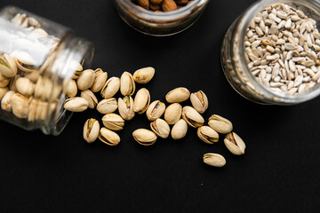Pistachio scattered on the black table from a jar. Walnut is a healthy vegetarian protein nutritious food.