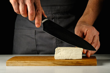 Chef cuts tofu cheese on a wooden board. High quality photo
