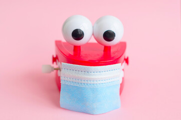 Fototapeta premium toy with smiling teeth and eyes with face mask on pink background as a concept of dentistry and healthy oral cavity and smile during pandemic