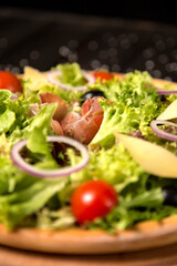Close up of Traditional Italian pizza with jamon Serrano in focus, Parmesan cheese, black olives and cherry tomatoes on wooden background. Tasty Mediterranean rustic meal. fast food delicious dish

