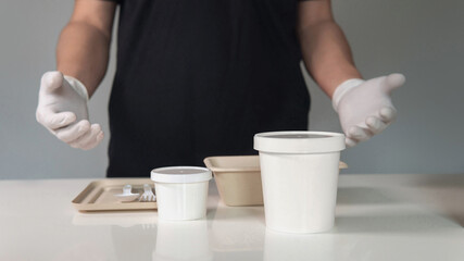 Environmentally friendly recyclable paper cup and plant fiber food packaging on white table with man wearing white latex gloves as a background. Healthcare concept and supporting small businesses