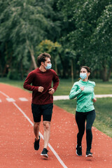 Couple in medical masks jogging together on running path in park