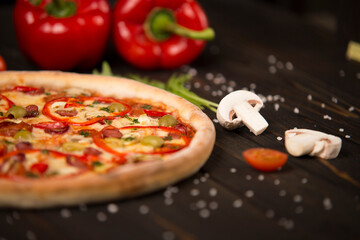 Half of pizza with bell pepper, green olives, sausages, mozzarella cheese, pepperoni, salami, chili pepper, champignons on wooden board with two bell peppers on background. Close up of uncut pizza
