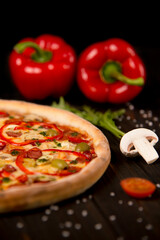 Half of pizza with bell pepper, green olives, sausages, mozzarella cheese, pepperoni, salami, chili pepper, champignons on wooden board with two bell peppers on background. Close up of uncut pizza

