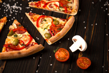 Close up of sliced pizza with bell pepper, olives, sausages, mozzarella cheese, pepperoni, salami, chili pepper on wooden board with sea salt, two tomatoes and champion on background. Rustic food
