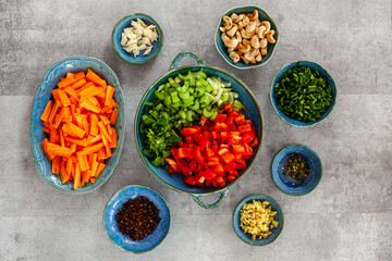 Various fresh cooking ingredients in bowls. Copy space, flat lay at gray background. Vegan cuisine ingredients, vegetables spices and nuts in round arrangement. Ready for stir-fry.