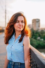 Portrait of a brunette girl with long hair on the background of a panorama of the city from the bridge at sunset