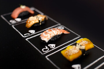 Hand drawn Poker cards, Japanese sushi nigiri with black rice and shrimp in focus on chalkboard. Near Asian food with salmon tataki, eel and Japanese omelette. Ebi nigiri between Unagi and Tomago