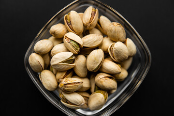 Pistachios in a small plate on a black table. Pistachio is a healthy vegetarian protein nutritious food. Natural nuts snacks.