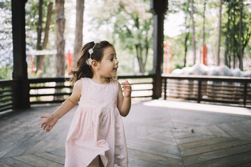 Little girl having fun in wooden gazebo in playground. Portrait of cute child running in wooden...