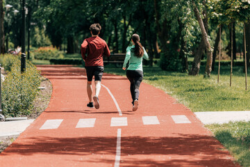 Back view of young couple jogging together on running track in park