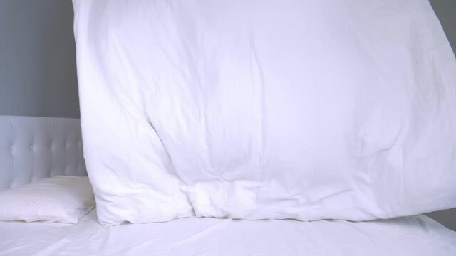 Young Caucasian Man Tidies Up White Sheets on Double Bed in Bedroom