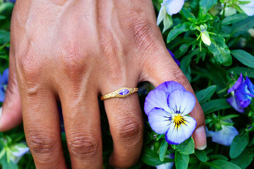 Hand wearing metal decorative ornamental ring with amethyst gemstone, touching plants