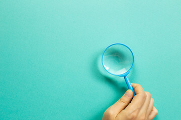 Hand holding a blue magnifying glass on green background. top view, copy space