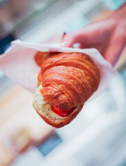 Croissant with tomato and cheese in hand, soft focus backgroud