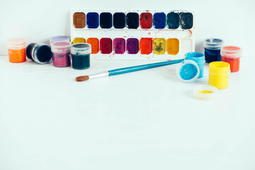 Colorful gouache paints and brush for painting on white wooden table. Copy, empty space for text
