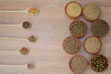 Different kinds of pelleted compound feed in bowls and spoons on wood table, copy space. Top view, flat lay