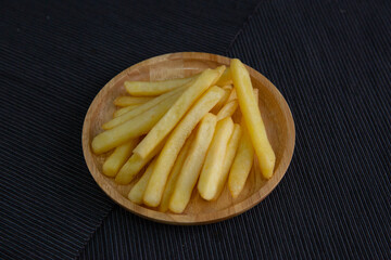French fries on a wooden plate on a black fabric floor