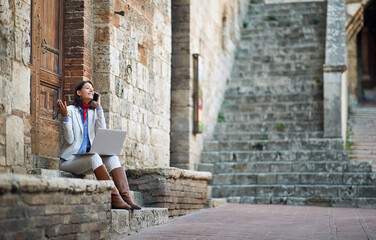 Fototapeta na wymiar young female talking on her cell phone with laptop, sitting outdoor on stairways in italy