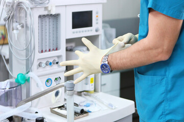 The doctor puts on gloves against the background of a ventilator. Unrecognizable photo. Copy of the space.