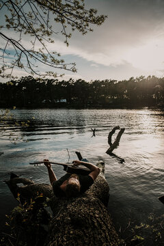 Man playing guitar while lying on tree trunk