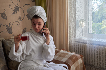 girl sitting on a sofa in a white bathrobe with a phone in her hand in a spa