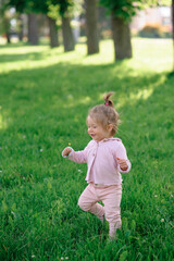 Little girl in casual clothes makes her first steps on the grass.