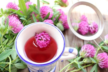 Herbal tea or infusion with red clover, purple flowers in a strainer, and on the wooden table. Natural floral background
