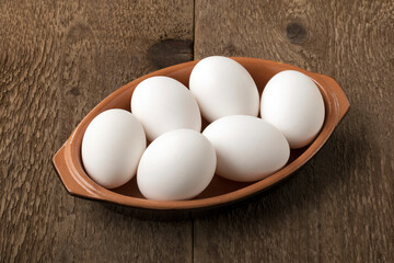 Six white eggs into a bowl on a wooden table.