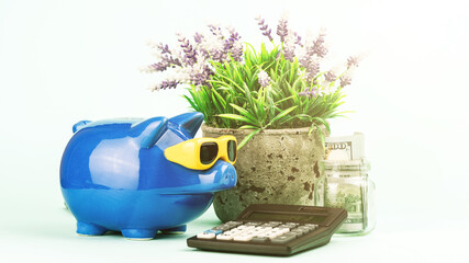 blue piggy bank leans on pot plant near old calculator
