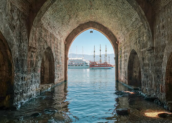 Fototapeta na wymiar View of pleasure tourist yachts through the stone arch of an old shipyard in Turkish Alanya in the afternoon