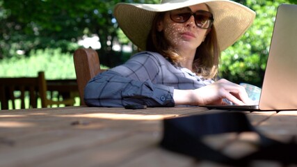 Fototapeta premium Woman in summer hat working at laptop outdoors in the holidays.
