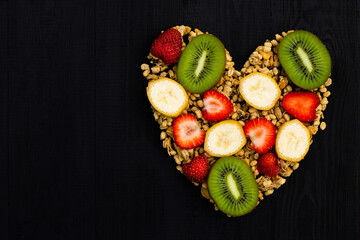 Obraz na płótnie Canvas Heart laid out of granola and fruits on black wooden background. Flat lay. Copy space.
