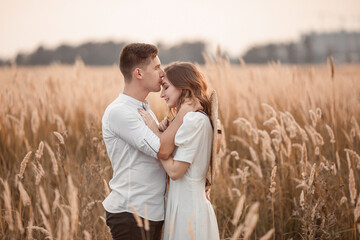 Happy lovers walk together and kiss in the field. A couple in love in a field at the end of summer. A brunette in a light dress and a straw boater hat. Love story.