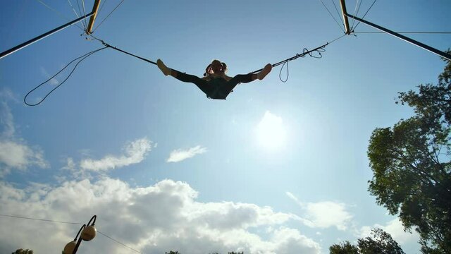 Teenage girl silhouette jumping on the trampoline bungee jumping. Slow motion video.