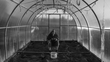 The girl in the greenhouse. A large round greenhouse in which the girl is located. A girl is sitting with a phone in her hands in a transparent greenhouse with vegetables