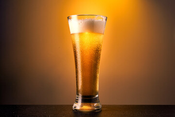 Cold craft light Beer in a glass with drops on a dark table. Pint of Beer on yellow color background.